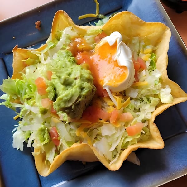 Taco salad in a crispy tortilla bowl with lettuce, guacamole, salsa, cheese, and sour cream.