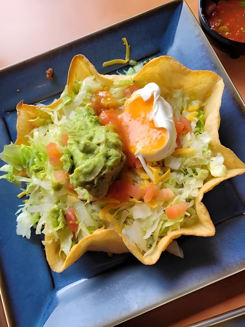Taco salad in a crispy tortilla bowl with lettuce, guacamole, salsa, cheese, and sour cream.