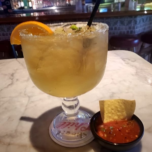 Margarita with orange slice and straw next to a bowl of salsa and a tortilla chip.