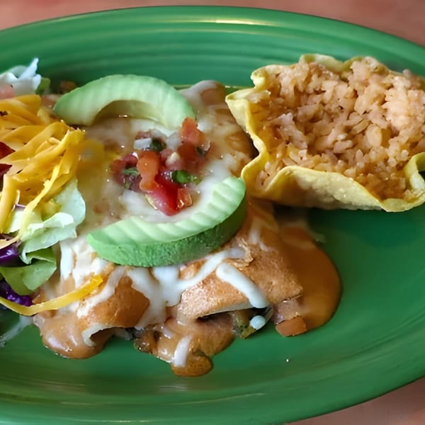 A green plate with enchiladas, rice in a tortilla bowl, and a side salad with cheese and avocado.