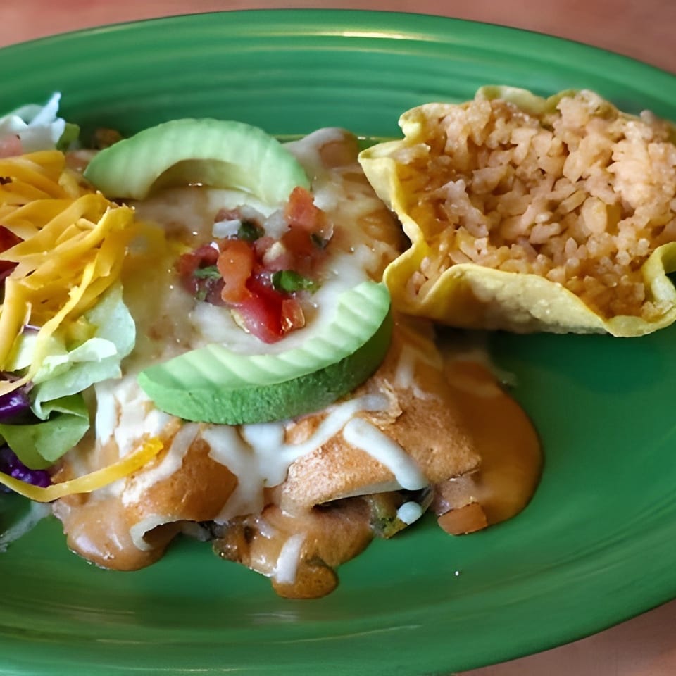 A green plate with enchiladas, rice in a tortilla bowl, and a side salad with cheese and avocado.