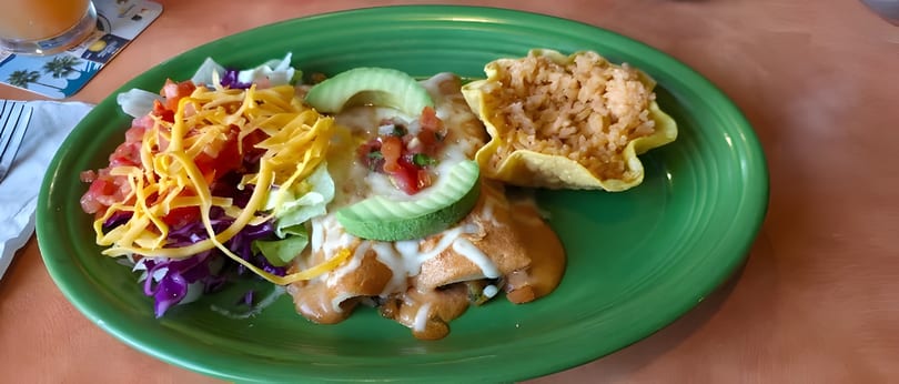 A green plate with enchiladas, rice in a tortilla bowl, and a side salad with cheese and avocado.