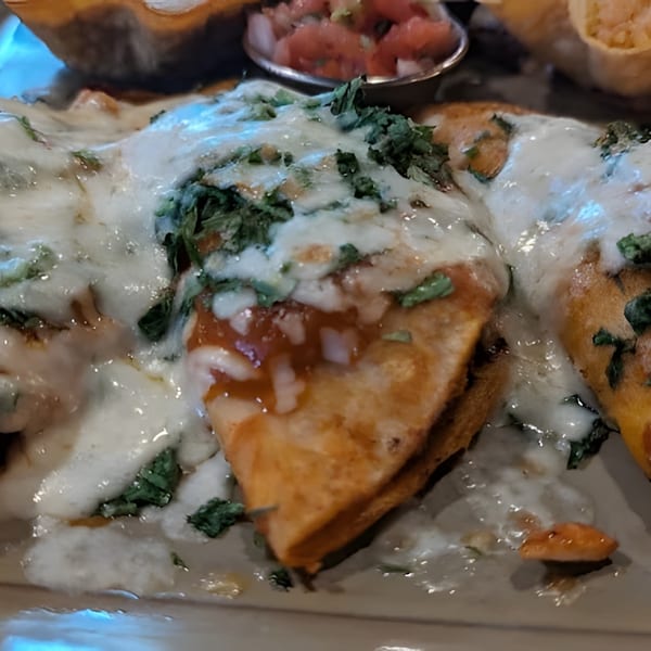 Three golden-brown enchiladas covered in melted white cheese, red sauce, and fresh green cilantro.