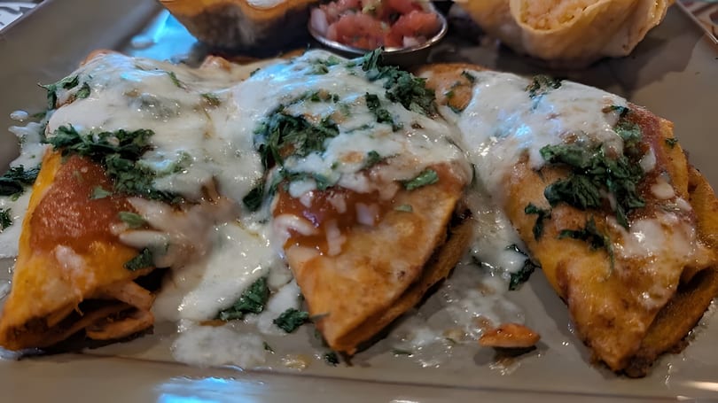 Three golden-brown enchiladas covered in melted white cheese, red sauce, and fresh green cilantro.