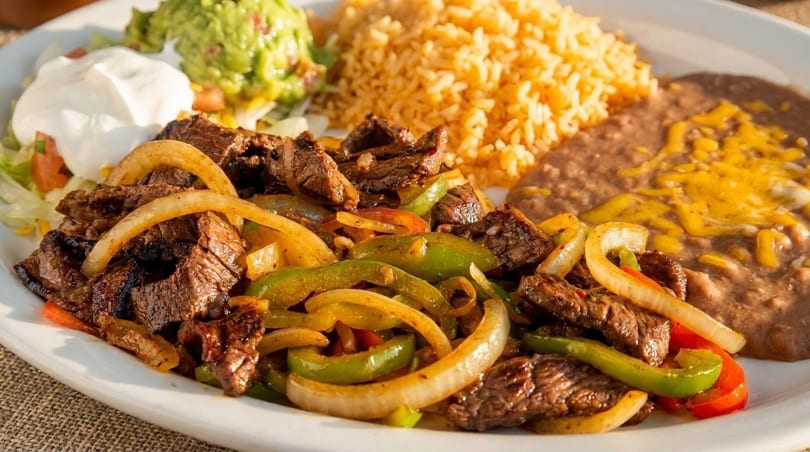 Steak fajitas with bell peppers and onions, served with rice, refried beans, guacamole, and sour cream.