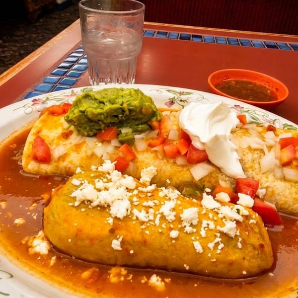 A plate of Mexican food with a burrito, tamale, guacamole, sour cream, and salsa.