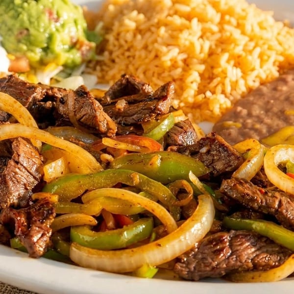 Steak fajitas with bell peppers and onions, served with rice, refried beans, guacamole, and sour cream.